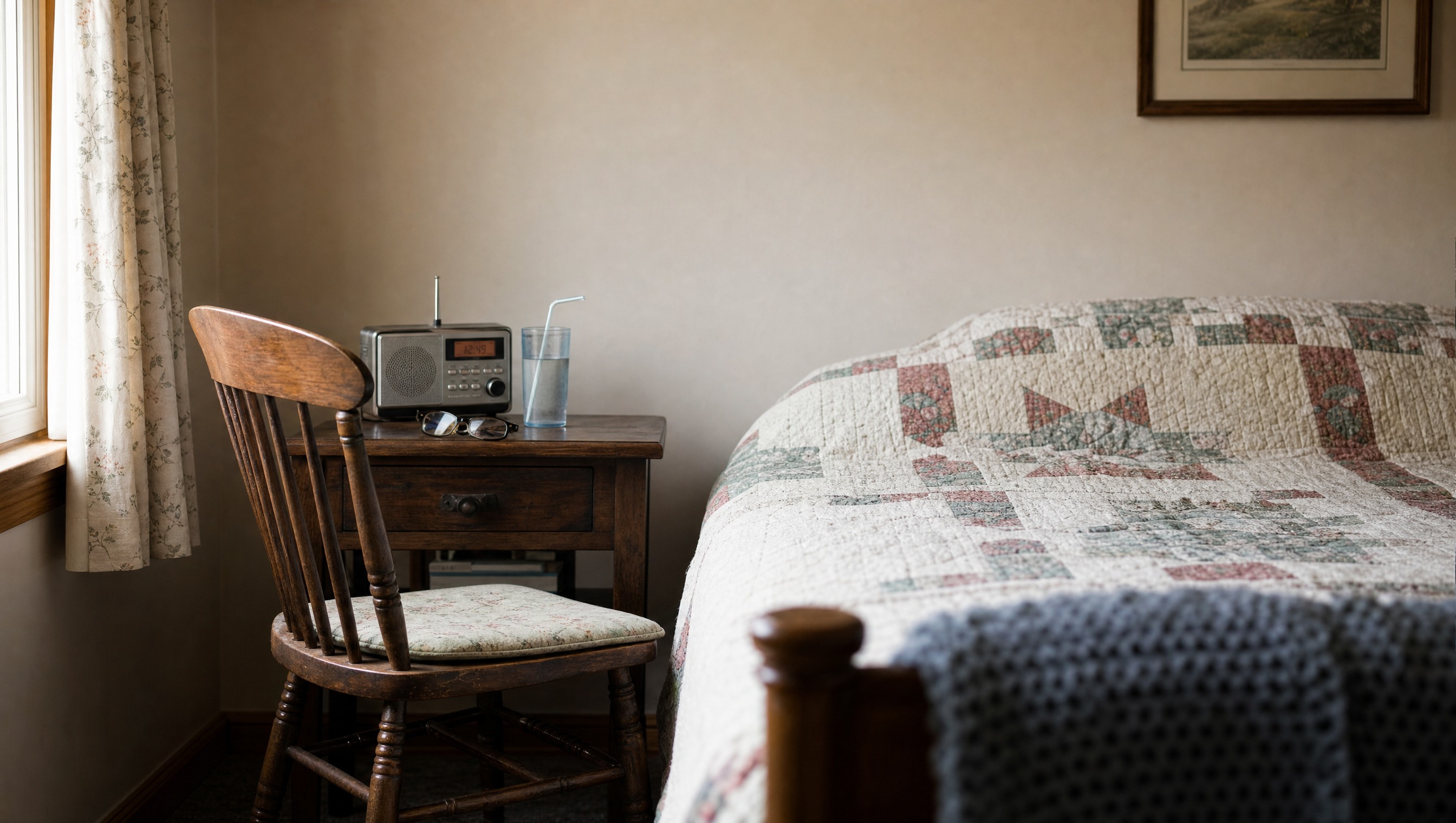 Chair pulled close to a bedside with a cup of water and a small radio on the nightstand